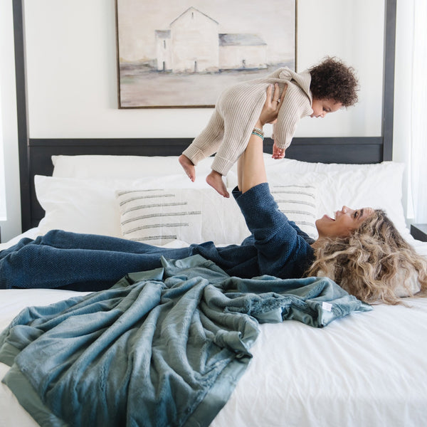 Mother and son playing together in bed laying on a teal toddler blanket. 