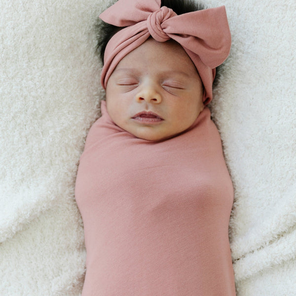 Newborn baby girl sleeping in rosy pink STRETCHY SWADDLE and matching bow headband- Saranoni