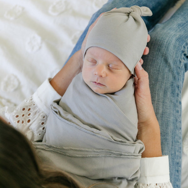 Mom rocking newborn baby in grey colored STRETCHY SWADDLES with matching hat- Saranoni