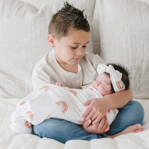 Older brother holding baby sister in soft and cozy STRETCHY SWADDLES in rainbow- Saranoni