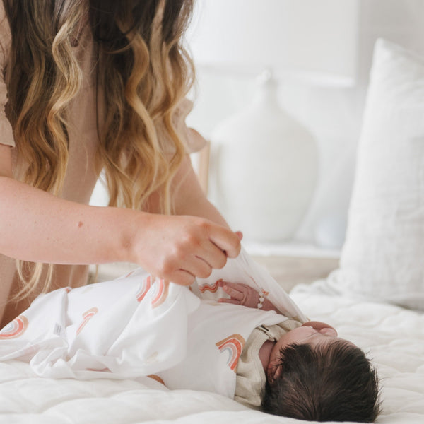 Mom wrapping newborn in rainbow pattern STRETCHY SWADDLES - Saranoni