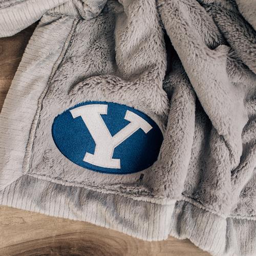 A Luxury Gray Colored Lush Saranoni Blanket. The soft blanket has a soft faux fur feeling. The blanket has the Brigham Young University Logo on it.