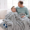 A father and son sit with Luxury Extra Large Throw Gray Colored Patterned Faux Fur Saranoni Blanket. The soft blanket is an oversized throw blanket and has a soft faux fur feeling. The blanket has a Brigham Young University Logo.