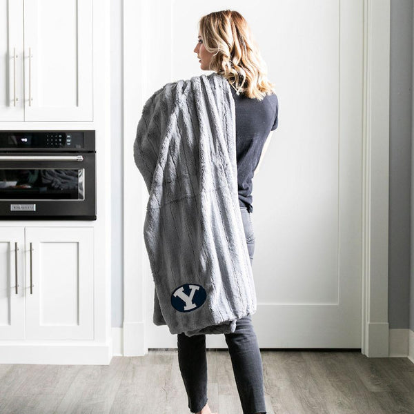 A woman holds a Luxury Throw Gray Colored Patterned Faux Fur Saranoni Blanket. The soft blanket is a throw blanket and has a soft faux fur feeling. The blanket has a Brigham Young University Logo.