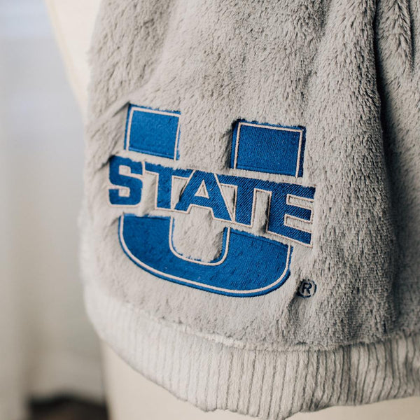 A Luxury Gray Colored Lush Saranoni Blanket. The soft blanket is a throw blanket and has a soft faux fur feeling. The blanket has the Utah State University Logo on it.