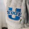 A Luxury Gray Colored Lush Saranoni Blanket. The soft blanket is a throw blanket and has a soft faux fur feeling. The blanket has the Utah State University Logo on it.