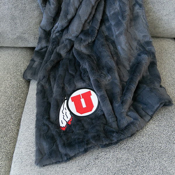 A Luxury Throw Charcoal Colored Patterned Faux Fur Saranoni Blanket. The soft blanket is a throw blanket and has a soft faux fur feeling. The blanket has a University of Utah Logo.