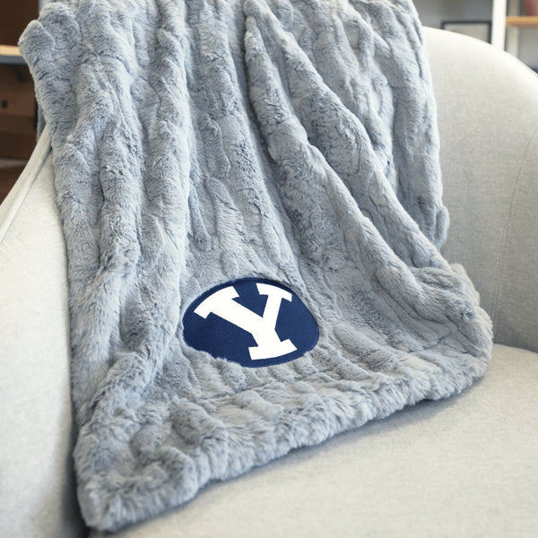 A Luxury Throw Gray Colored Patterned Faux Fur Saranoni Blanket. The soft blanket is a throw blanket and has a soft faux fur feeling. The blanket has a Brigham Young University Logo.