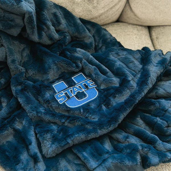 A Luxury Throw Midnight (dark blue) Colored Patterned Faux Fur Saranoni Blanket. The soft blanket is a throw blanket and has a soft faux fur feeling. The blanket has a Utah State University Logo on it.