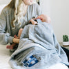 A mother holds her baby while holding a Luxury Receiving Gray Colored Lush Saranoni Blanket. The soft blanket is a toddler blanket or baby blanket and has a soft faux fur feeling. The blanket has the Utah State University Logo on it.