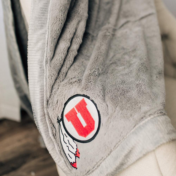 A Luxury Gray Colored Lush Saranoni Blanket. The soft blanket has a soft faux fur feeling. The blanket has the University of Utah Logo on it.