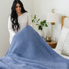 Intricate details of a blue-colored waffle knit king blanket draped across a bed. 