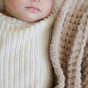 Detailed view of a baby snuggling next to the intricate waffle weave pattern of a tan mini blanket.