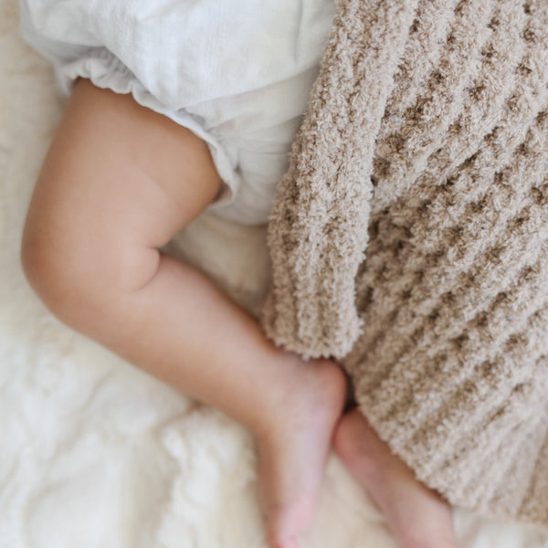 Detailed view of a baby snuggling next to the intricate waffle weave pattern of a tan mini blanket.