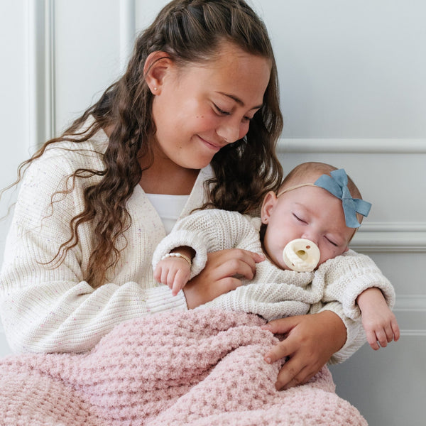 Young girl holding baby girl both snuggled in cozy pink waffle knit blanket.