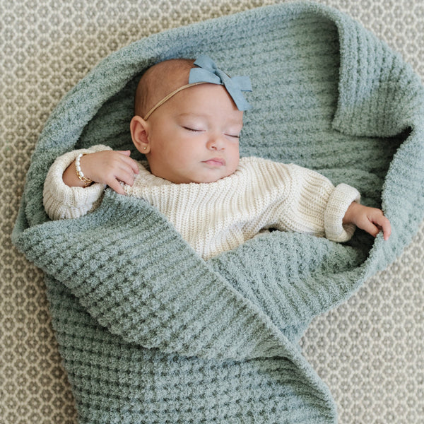 Baby girl asleep wrapped up in blue waffle knit blanket.