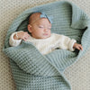 Baby girl asleep wrapped up in blue waffle knit blanket.