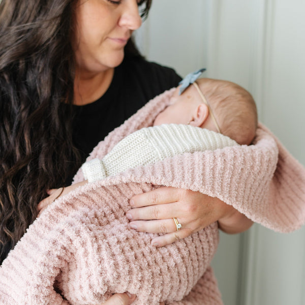 Mom holding daughter wrapped up in pink waffle knit blanket.