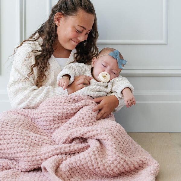 Young girl holding baby girl both snuggled in pink receiving waffle knit blanket.