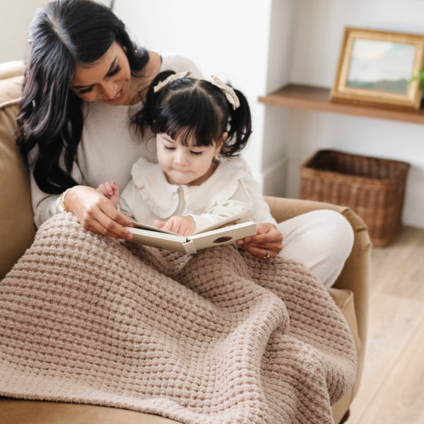 Mom and daughter reading together on couch snuggled up with their favorite tan waffle knit blanket.