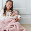 Young girl holding baby girl both snuggled in pink receiving waffle knit blanket.