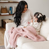 Mom and daughter sitting on couch snuggling up with receiving pink waffle knit blanket. 