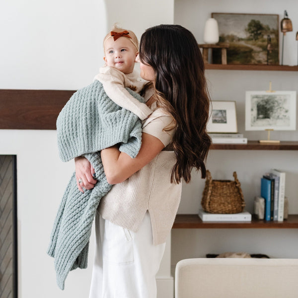 Mom holding daughter snuggled up in blue waffle knit receiving blanket.