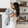 Mom holding daughter snuggled up in blue waffle knit receiving blanket.