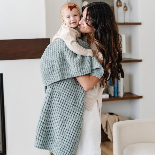 Mom holding baby daughter snuggled up in blue waffle knit receiving blanket.