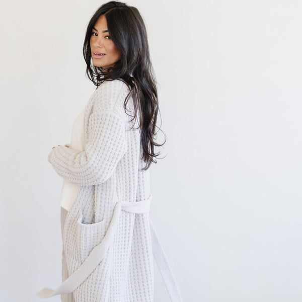 Woman standing in a light gray waffle knit robe enjoying a peaceful morning. 