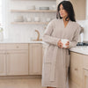 Woman wearing a beautifully colored waffle knit robe, leaning against the kitchen counter.