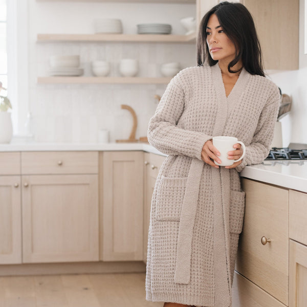 Woman standing by the stove in a beige waffle knit robe, enjoying a peaceful morning.