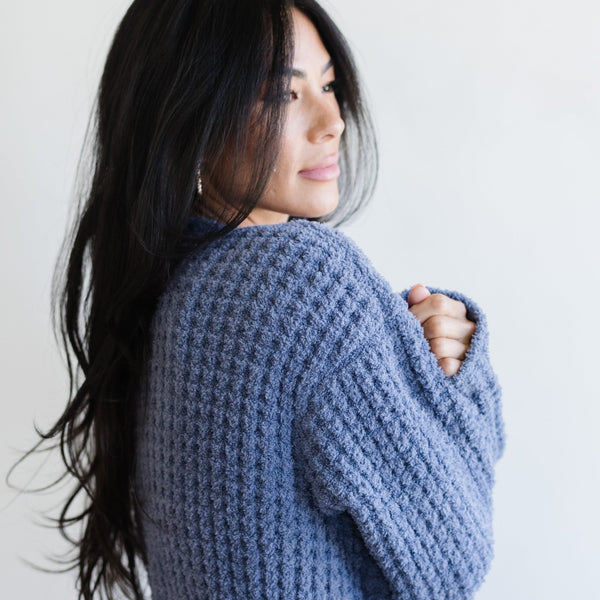 Woman snuggling up wearing blue waffle knit robe. 