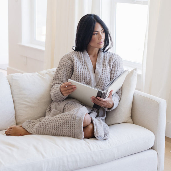 Woman sitting on couch wrapped in gray waffle knit robe.