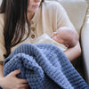 Detailed shot of baby laying in mother's arms, wrapped in blue waffle knit blanket. 