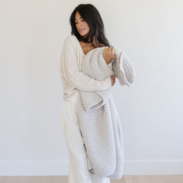 Woman snuggling up to light gray waffle knit blanket.