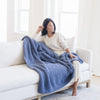 Person cozily wrapped in a blue waffle knit throw blanket, sitting on a couch..