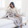 Woman relaxing on couch snuggled up with a light gray waffle knit blanket.