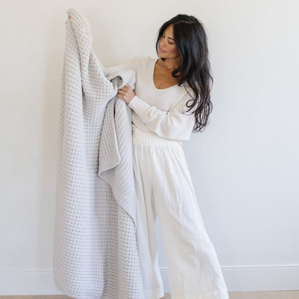 Woman holding up a light gray waffle knit throw blanket.