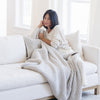 Person cozily wrapped in a gray waffle knit throw blanket, sitting on a couch.