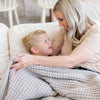 Mother and son enjoying time together on couch while wrapped in light gray waffle knit throw blanket.