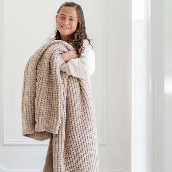 Close-up of young girl cuddling with Wheat Waffle Knit Toddler blanket showing its textured pattern - tan colored Waffle Knit blanket