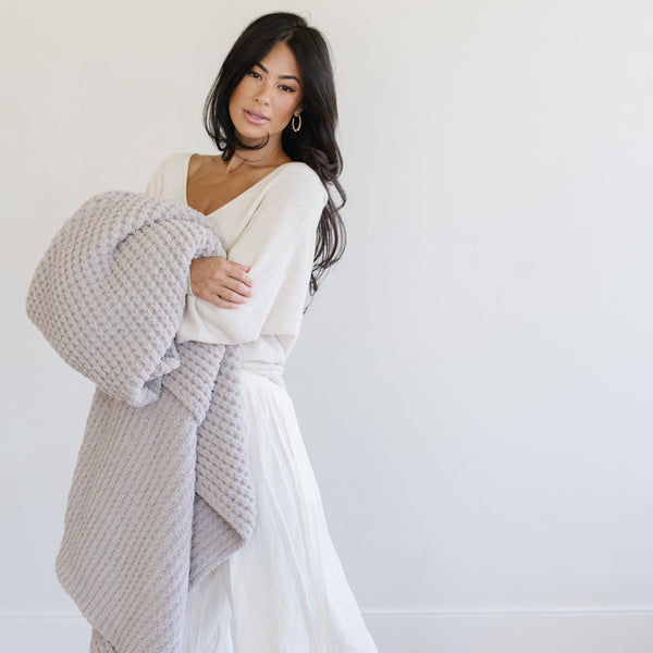 Woman holding a light gray waffle knit blanket.