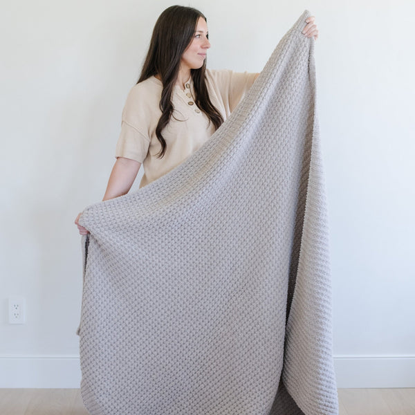 Woman holding up a homey, light grey XL waffle knit blanket.